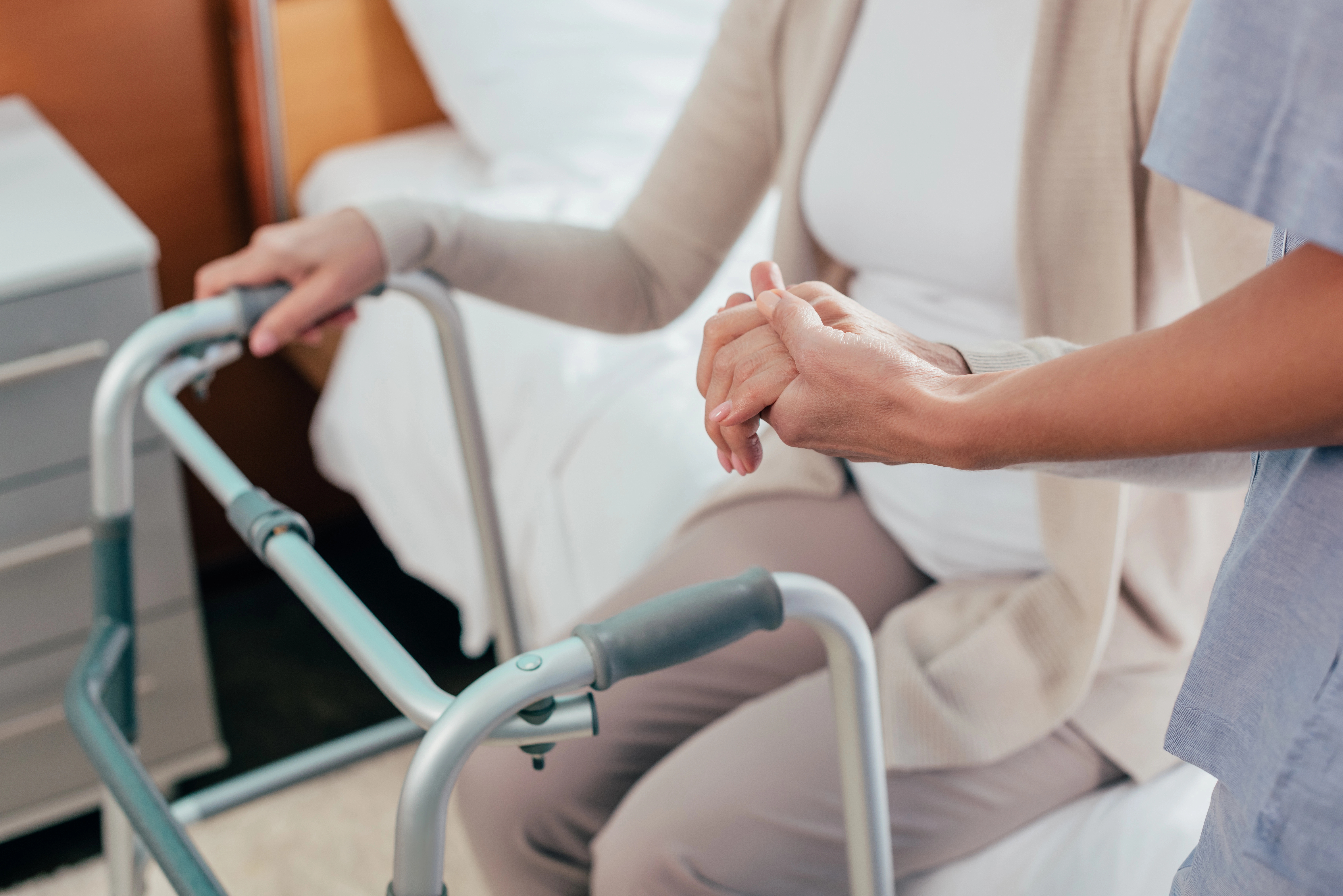Caregiver holding an older person's hand on a walker